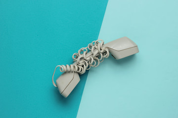 Handset wrapped cable on blue paper background. Minimalistic office concept. Top view
