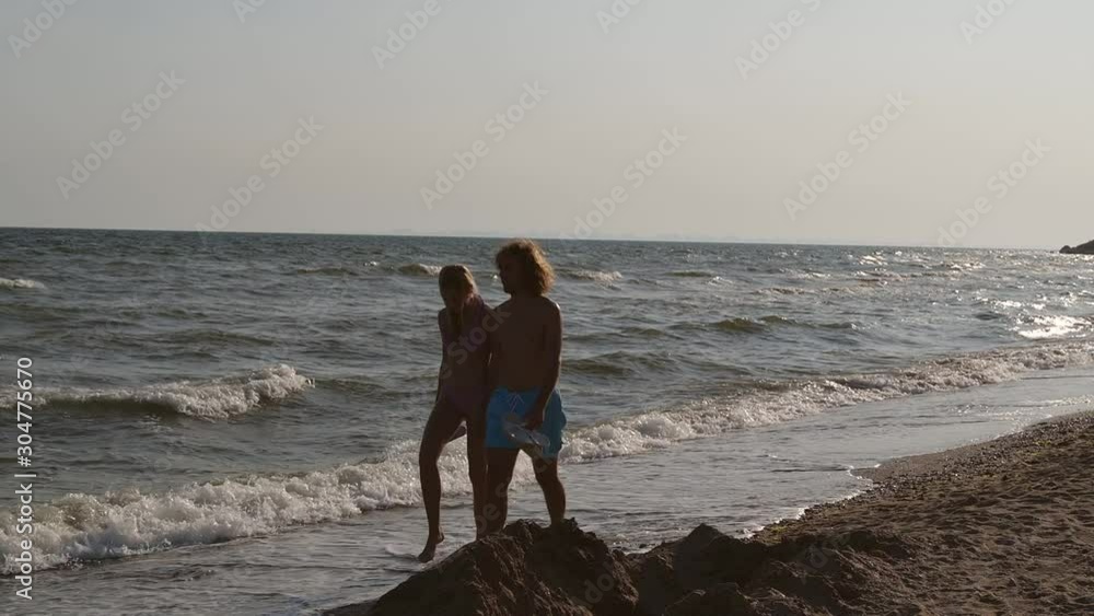 Poster Young couple walking on beach at sunset