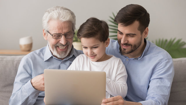 Cute little boy with father and happy grandfather using laptop