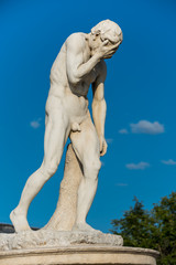 Cain Statue in Tuileries Garden in Paris, one of many statues in the Tuileries Garden. It shows a naked man (Cain) standing or propped awkwardly with his right hand covering his face.