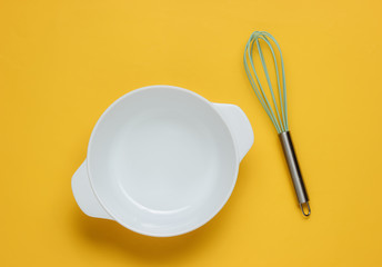 Cooking concept. Empty white bowl with whisk on yellow studio background. Top view.