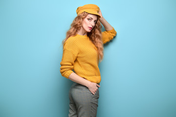 Naklejka premium Fashionable woman in Trendy orange outfit, stylish hairstyle, makeup. Young redhead in jumper, yellow cap. Sensual beautiful model girl in stylish pants, fashion beauty concept on blue