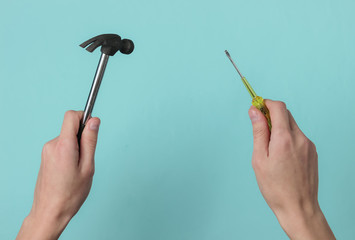 Repair concept. Female hand holds a screwdriver and a hammer on blue studio background.