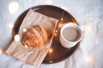 Fresh pastry with hot cup of coffee in bed closeup over lights. Good morning. Selective focus.