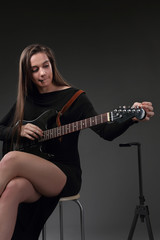 Beautiful girl tuning strings on electric guitar