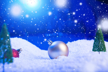Christmas background with Christmas balls on snow over fir-tree, night sky and moon. Shallow depth of field. Christmas background. Fairy tale. Macro. Artificial magic dreamy world.