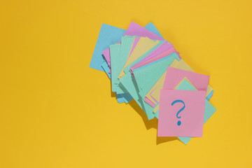 Minimalistic office concept. Lot of memo papers with question mark on yellow background. Top view