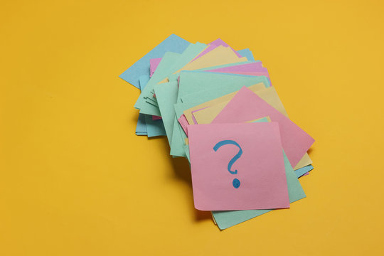 Minimalistic office concept. Lot of memo papers with question mark on yellow background. Top view