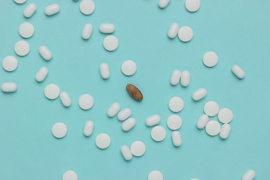 Lot of white pills and one herbal pill on a blue background.