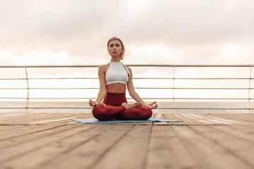 Fototapeta na wymiar Practice yoga in the morning outdoors. Young woman yogi in sportswear is sitting in lotus position on the beach at sunrise. Inner harmony