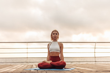 Fototapeta na wymiar Practice yoga in the morning outdoors. Young woman yogi in sportswear is sitting in lotus position on the beach at sunrise. Inner harmony