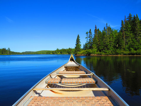 Canadian rabaska canoe resting by the calm water in beautiful  Wapizagonke lake. Mauricie National Park, Quebec Canada.Look out point with blue sky and tranquil waters landscape