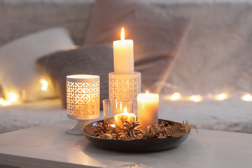 Obraz na płótnie Canvas Christmas decoration with burning candles on white table against the background of sofa with plaids and pillows. Cozy home and holiday concept