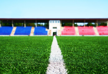 Green lawn of a soccer field on the background of the stands in a summer sunny day.