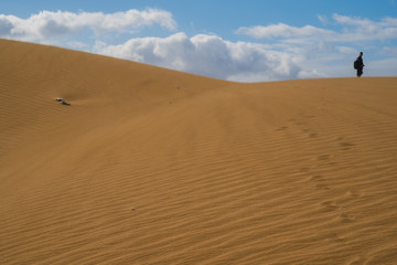 Person is walking on sand dunes during sunny and windy day in the Natural Reserve of Dunes of Maspaloma in Gran Canaria with sand dust  and foot steps. Canary Islands, Spain