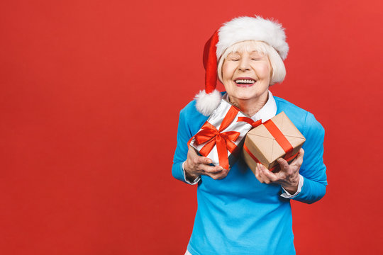 Happy mature woman with a gift. Isolated over red background. Beautiful stylish senior lady opening her Christmas gift. Elegant mature woman holding a red gift box.