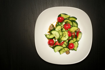 Salad on a white plate on black wood.