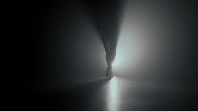 Dancer's legs in dark in smoky room of nightclub. Girl dances beautifully and seductively to beat of music. Slow motion.