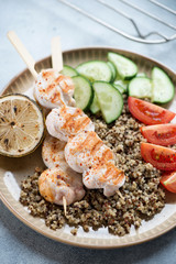 Beige plate with fried chicken fillet on skewers, quinoa and fresh vegetables, closeup, vertical shot