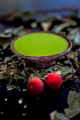 Close up shot of banyan tree paste in a clay bowl on black wooden surface along with some raw and...