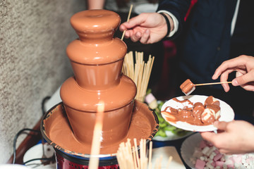 Fototapeta na wymiar Vibrant Picture of Chocolate Fountain Fontain on a children kids birthday party with a kids playing around and dipping marshmallows and fruits into the fountain