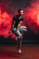 portrait of vigorous dancer male dancing street dance, jump in the air isolated over smoky background