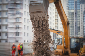 Yellow heavy excavator excavating sand and working during road works, unloading sand during construction of the new road