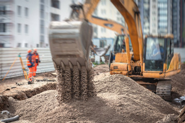 Yellow heavy excavator excavating sand and working during road works, unloading sand during...