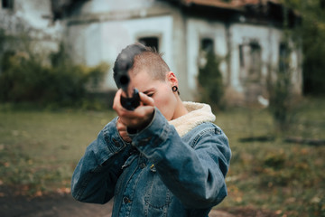 Young woman with short hair and a punk style, holds an old double-barrel shotgun in an abandoned estate. She is pointing at the camera.