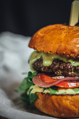 Homemade grilled beef burger with blue cheese and rucola served on wooden plate on dark background