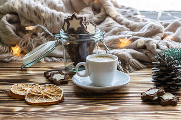 Festive Christmas composition in hygge style with cup of hot aromatic coffee, homemade chocolate cookies, warm blanket and decor on rustic wooden table.