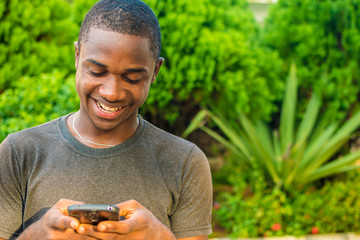 Fototapeta premium handsome young african man viewing content on his mobile phone, smiling while typing and surfing the internet
