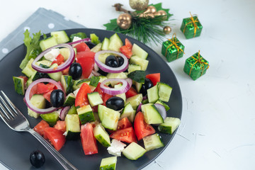 Greek salad. Diced tomatoes, cucumbers, feta cheese, olives. Rings of red onion. Food for vegetarians. Festive and New Year's dish. On a light background. Copy space. 