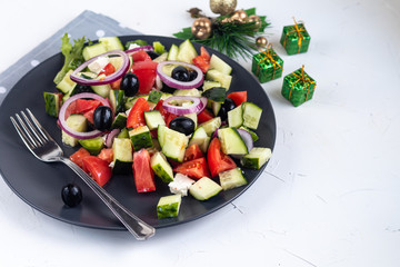 Greek salad. Diced tomatoes, cucumbers, feta cheese, olives. Rings of red onion. Food for vegetarians. Festive and New Year's dish. On a light background. Copy space. 