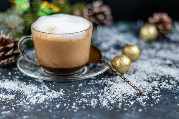 Cappuccino in a transparent cup with white, milk froth. New Year decorations, Christmas tree branches. Festive mood. Copy space. 