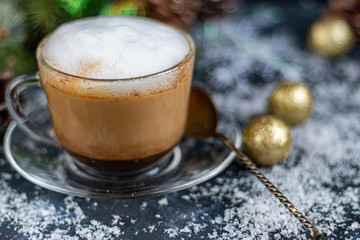 Cappuccino in a transparent cup with white, milk froth. New Year decorations, Christmas tree branches. Festive mood. Copy space. 