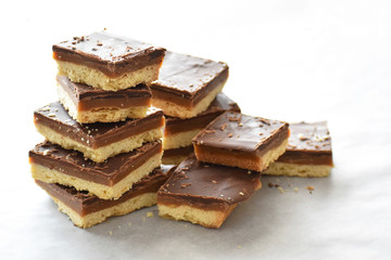 Millionaire's shortbread with chocolate and caramel on a parchment paper with copy space on the right side.