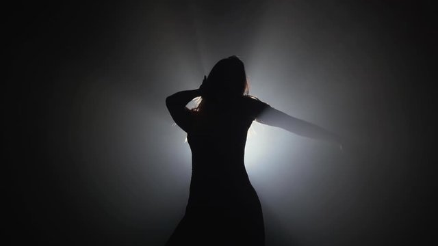 Slim sexy woman dancing on smoke dark stage in front of light projector. Concept of arts, flexibility, talented girl.
