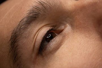 Young attractive man eye close-up with the master hand in black gloves and permanent makeup machine with a needle. Male permanent makeup procedure.