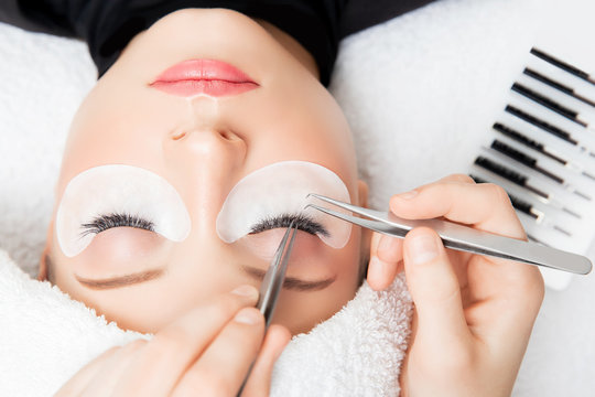 Eyelash extension procedure. Master tweezers fake long lashes beautiful female eyes