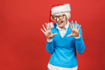 Senior aged grey-haired woman wearing Christmas Santa hat over isolated red background very happy...