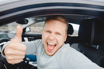 Driver of car takes selfie photo, shows thumb up from window. Man smiles, mouth wide open, sunlight. Travel rental concept