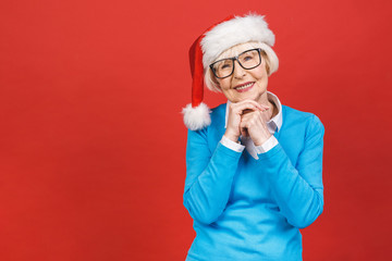 Senior aged grey-haired shoked, wearing Christmas Santa hat over isolated red background very happy and excited, having fun, smiling.