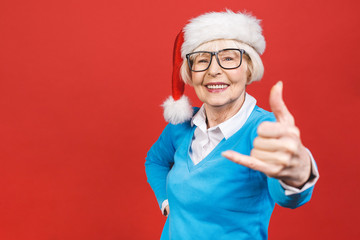 Fototapeta na wymiar Senior aged grey-haired woman wearing Christmas Santa hat over isolated red background very happy and excited, having fun, smiling. Happy winner.