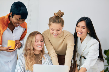 Caucasian and african female work together in office using laptop, discussing business ideas, share experience with each other. Success and leadership, togetherness concept