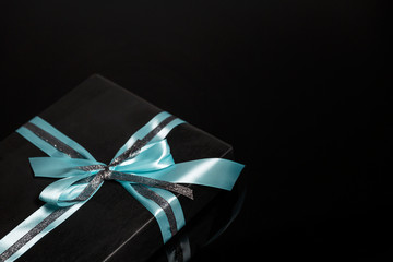 Black gift box with a turquoise bow on a black background. Card. Space for text.