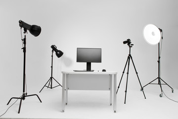 Photographer working place in photo studio with lighting equipment. Camera on the tripod. PC computer on desk. Designer working place.