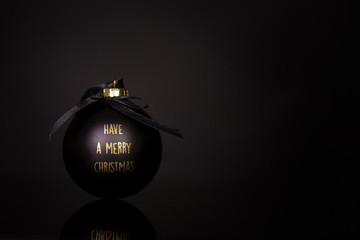 Black Christmas ball with congratulations in gold letters on a black background. Space for text. Close-up.