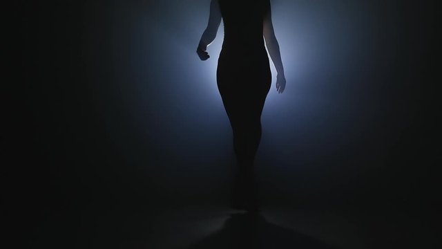 Slim sexy woman dancing on smoke dark stage in front of light projector. Concept of arts, flexibility, talented girl.