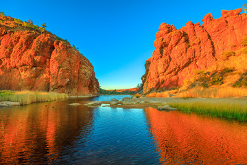 Northern Territory, Australian Outback. Scenic Glen Helen Gorge in West MacDonnell Ranges changes colours with sunrise light and reflects on waterhole in dry season at sunrise light.